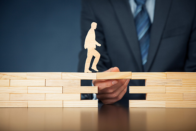 photo of a man walking across an unsettled bridge of blocks, supported by a coach